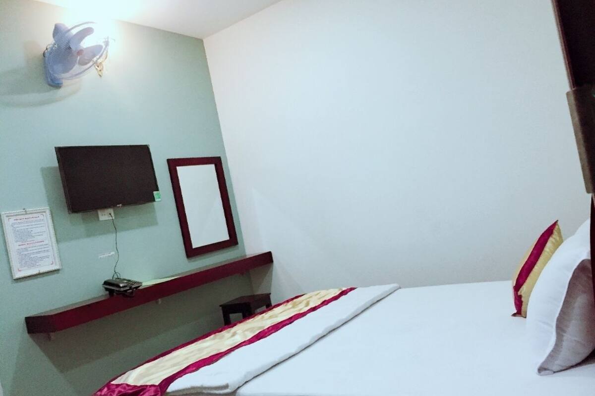 Une chambre d’hôtel avec un lit, un téléviseur fixé au mur, une petite table et un ventilateur fixé au mur.