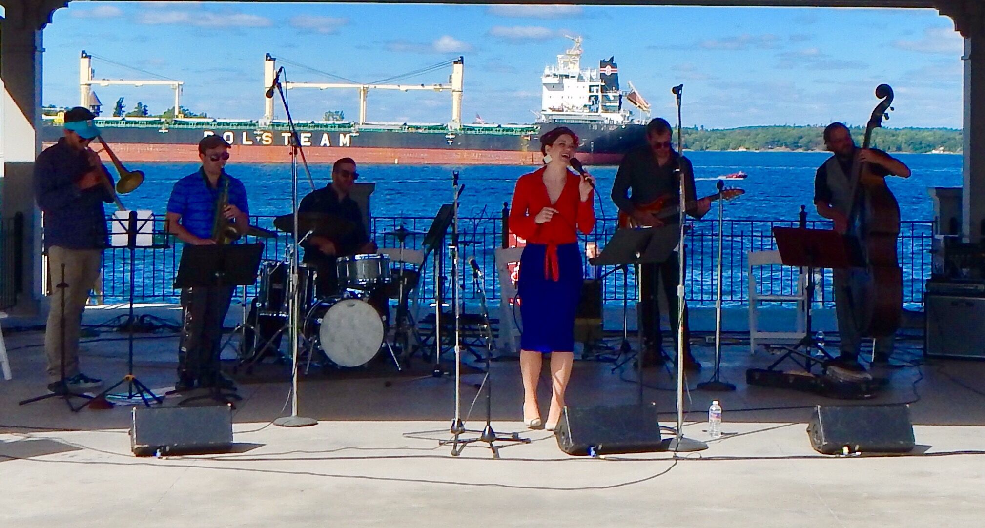Een band treedt op op een podium, met een schip op de achtergrond.
