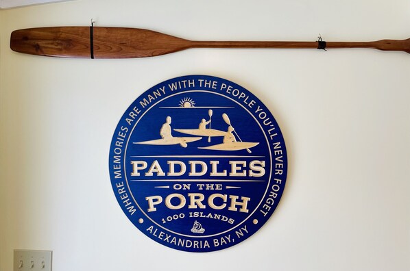 A circular sign with the text "PADDLES ON THE PORCH" and "1000 Islands, Alexandria Bay, NY". - Alexandria Bay, 1000 Islands Waterfront Cottage For Rent directly on the water, (Alexandria Bay)
