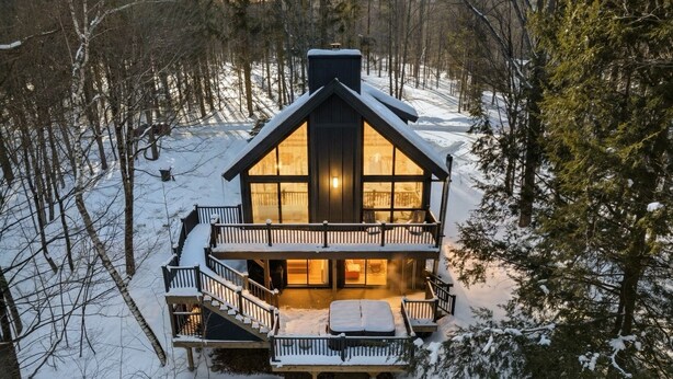 Een chalet met twee verdiepingen, een balkon en een zichtbare open haard van binnenuit.