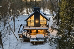 Uma cabana de dois andares com uma varanda e uma lareira visível no interior.