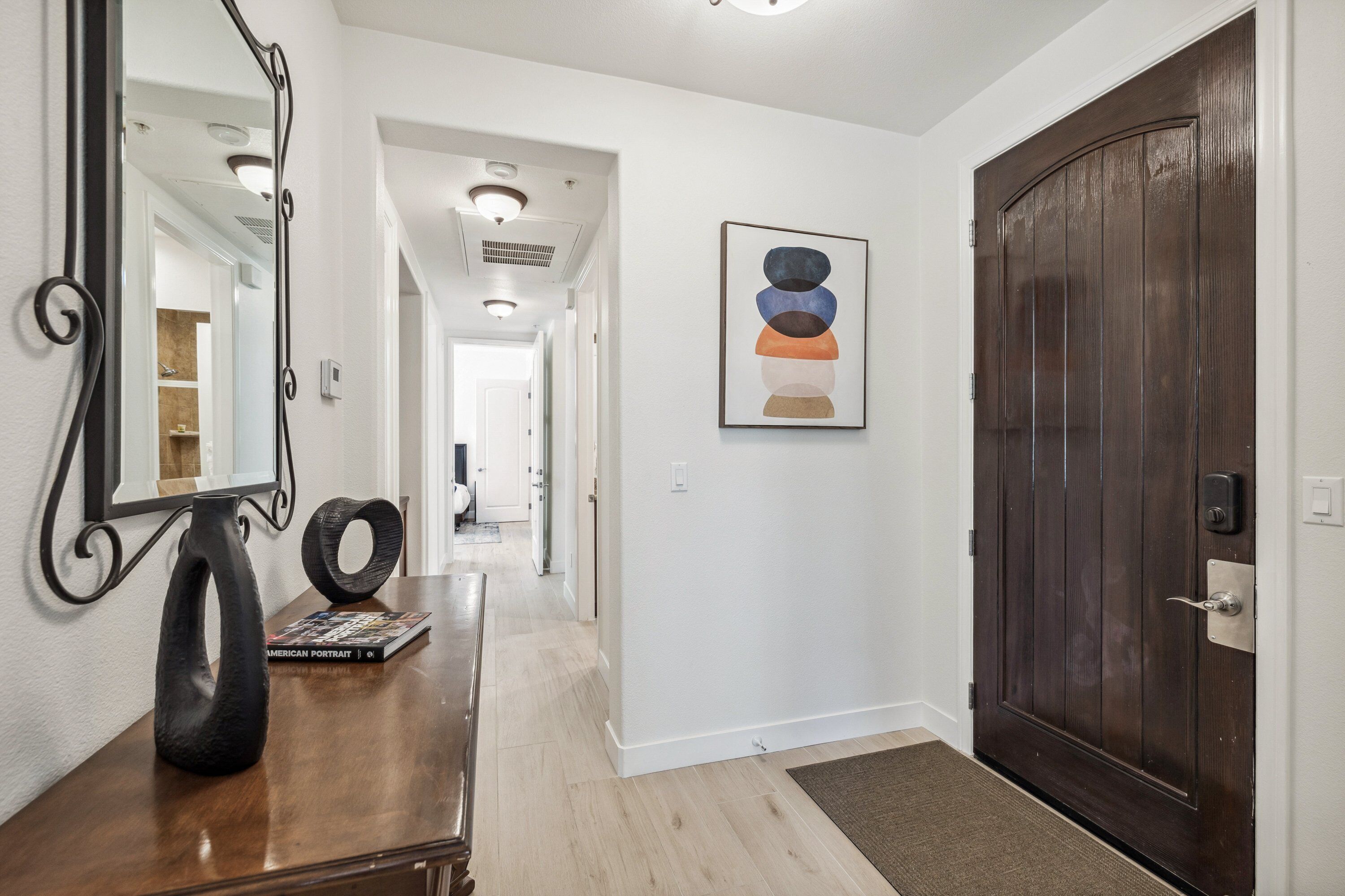 A hallway with a wooden dresser, a mirror, and a framed abstract painting.