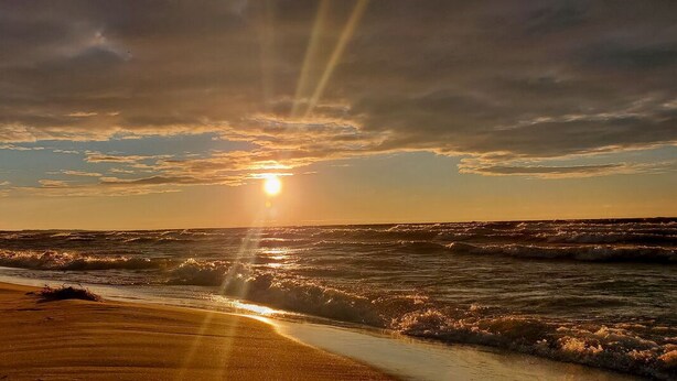 Ein Strand mit Wellen und einem Sonnenuntergang.
