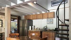 Une cuisine avec des meubles en bois, un réfrigérateur en acier inoxydable, une table ronde en verre et un escalier en colimaçon.