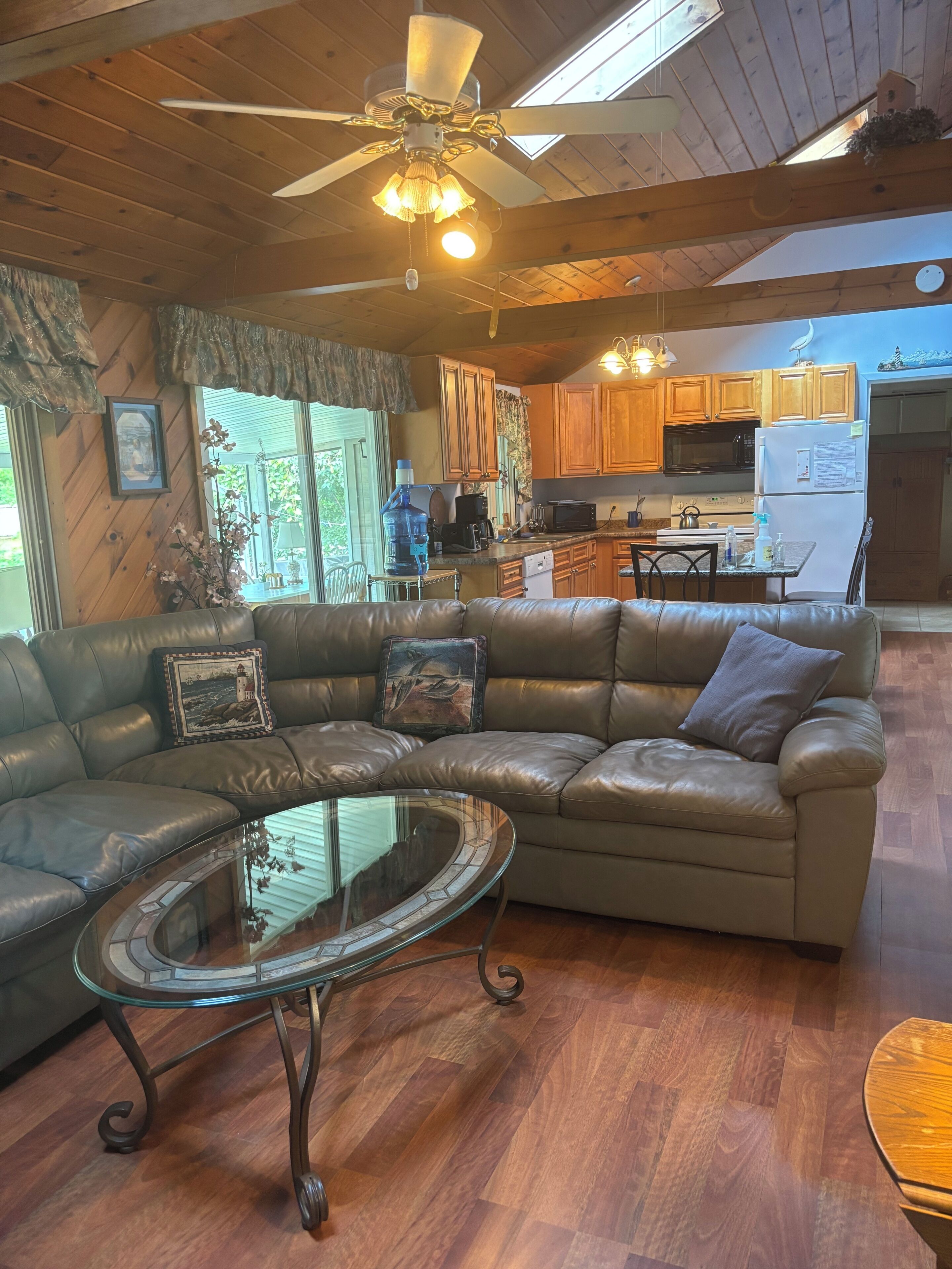 A living room with a leather sectional sofa, a glass coffee table, and a ceiling fan.
