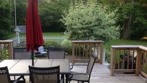 Une terrasse en bois avec une table et des chaises, entourée d’une clôture blanche en bois et de verdure.