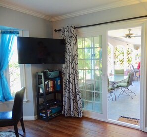 Una sala de estar con televisor de pantalla plana, una estantería y una puerta corrediza de vidrio que da a un patio exterior con mesa y sillas.