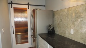 Cocina compacta con refrigerador de acero inoxidable, encimera negra y piso de madera.