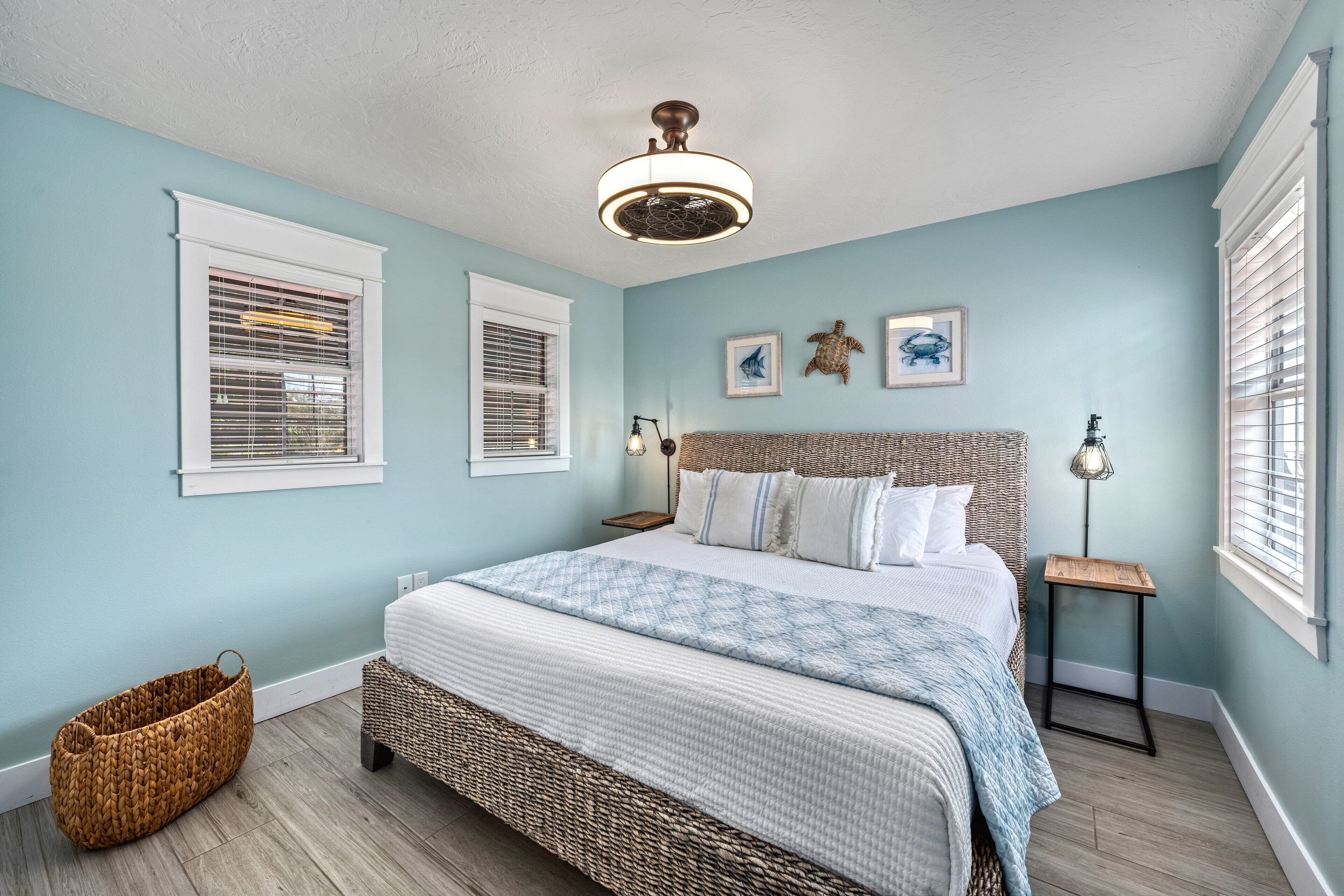 A bedroom with a large bed, two bedside tables, a wicker basket, and a ceiling fan.