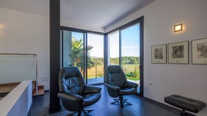 A modern room with two leather chairs, a bench, and large windows offering a view of greenery. - Modern Villa with pool close to IBIZA. (IBIZA)