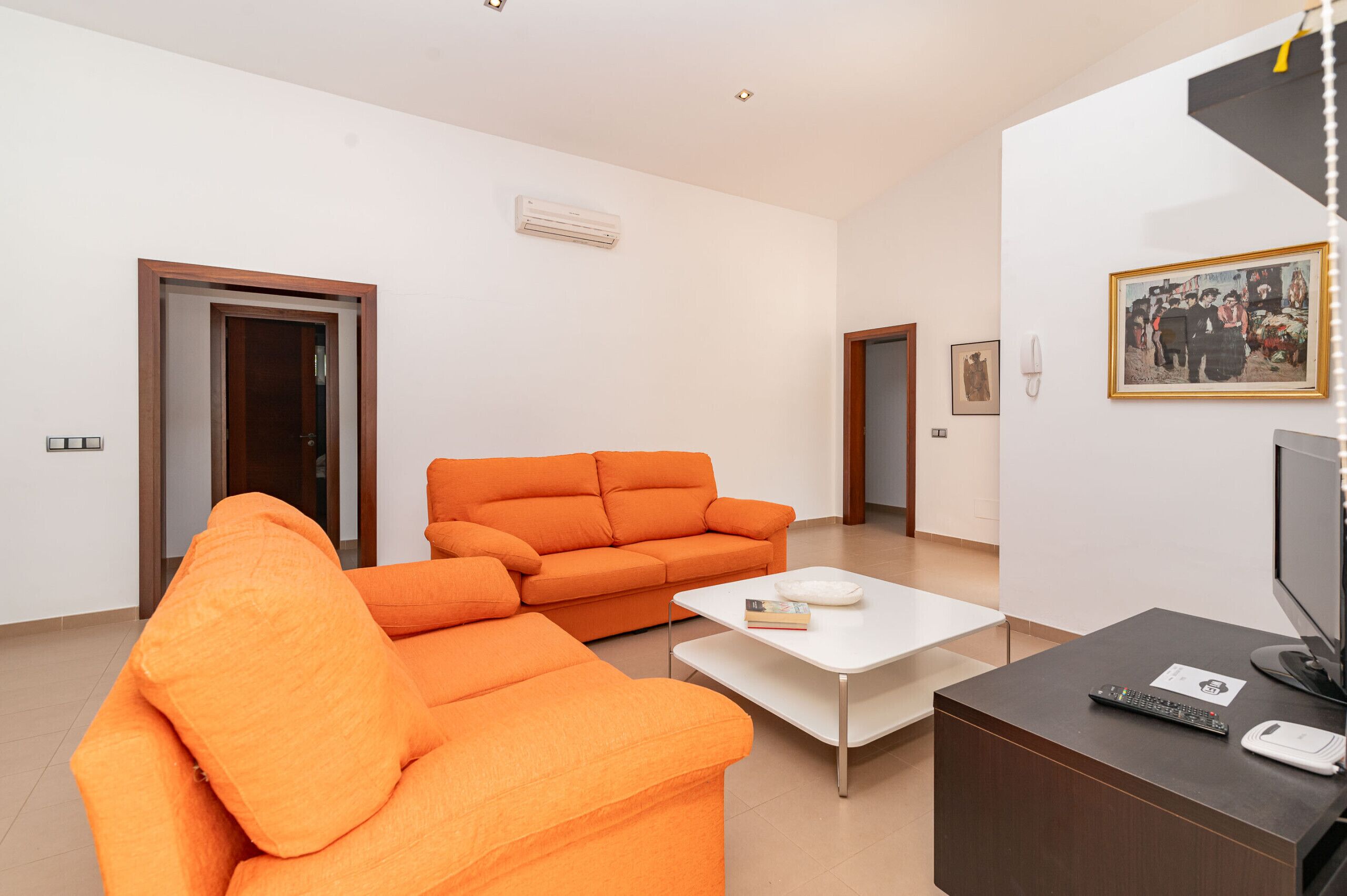 En moderne stue med en stor orange sofa, et hvidt sofabord og et fjernsyn på et træstel.