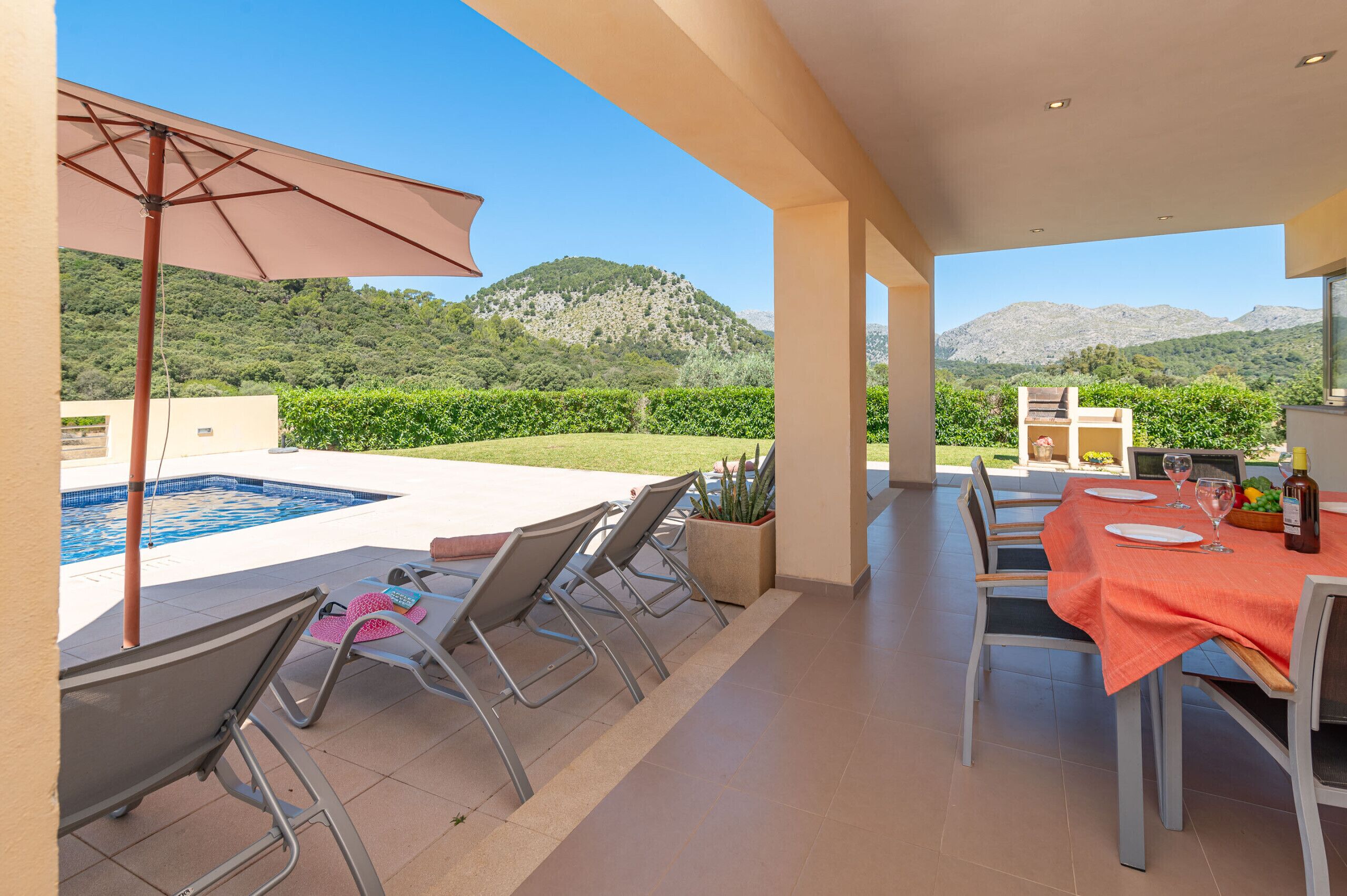 Un patio con piscina, sillas y una mesa lista para comer, con vistas a un paisaje montañoso.