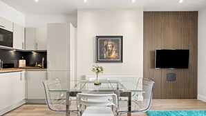 A modern kitchen with white cabinets, a glass dining table, and a framed artwork on the wall. - Comfy Modern 2-Bed Notting Hill Portobello Apt (London)