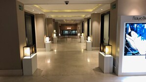 En hotelgang med et moderne design, med en central passage omgivet af oplyste udstillingsmontre og en stor digital reklame på højre side.
