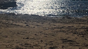 En strand med en klippefyldt kystlinje og en person, der står nær vandet.