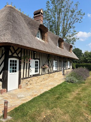 A traditional half-timbered house with a thatched roof, stone foundation, and a stone pathway leading to the entrance.
