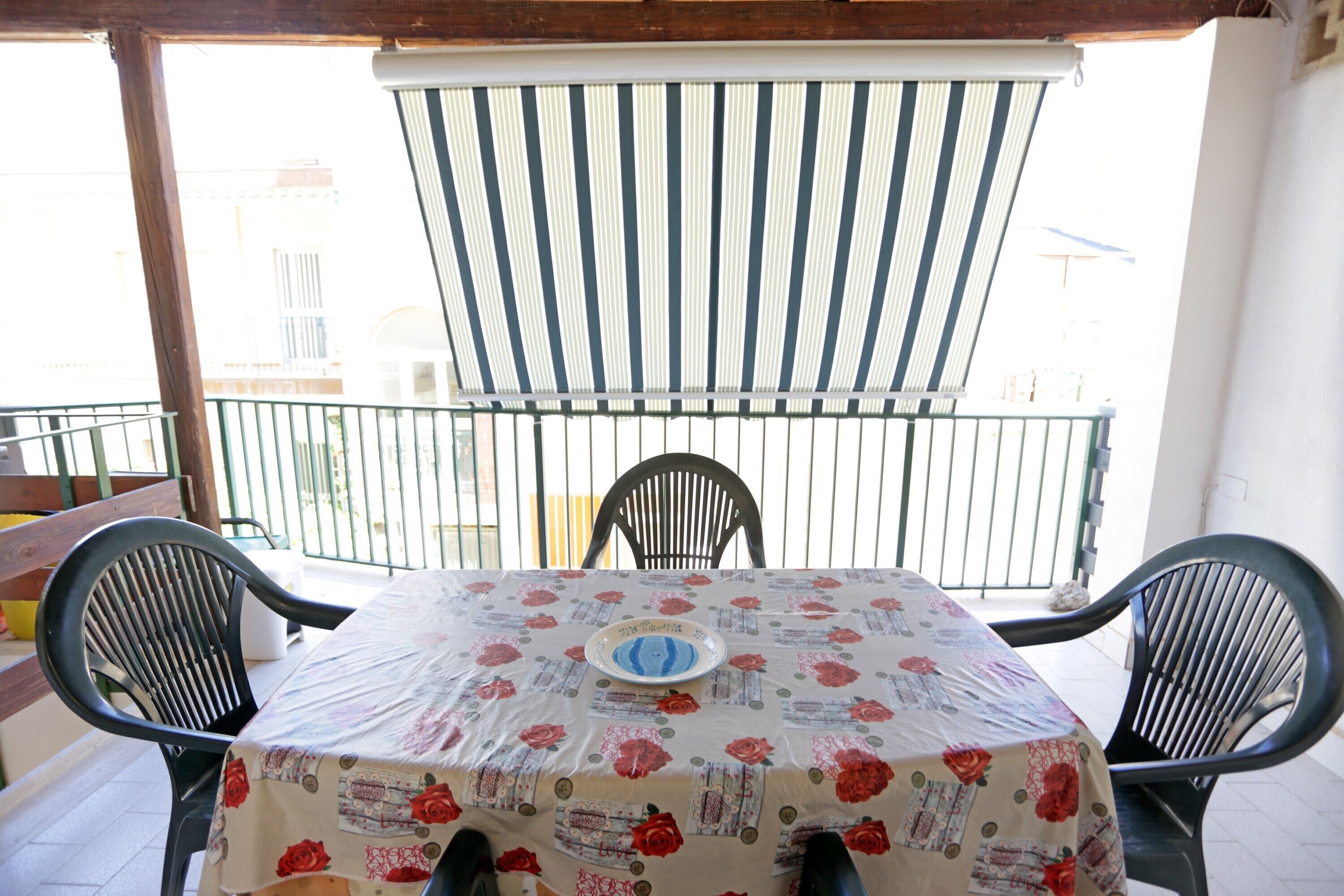 A balcony with a table covered in a floral tablecloth, two black chairs, and a striped awning.