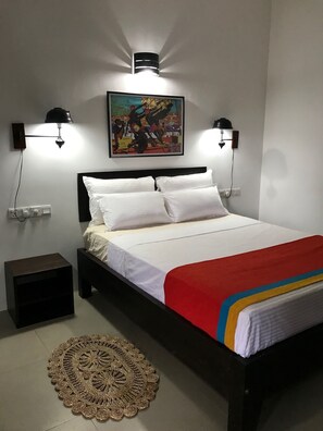 A neatly made bed with white linens and a red blanket, two wall-mounted reading lamps, a framed picture above the bed, a small bedside table, and a decorative rug on the floor. - Blue Pillars Kandy (Kandy)