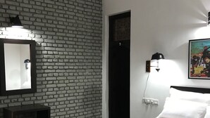 A bedroom with a brick-patterned wall, a bed with a colorful bedspread, a nightstand, a mirror, and a wall-mounted lamp. - Blue Pillars Kandy (Kandy)
