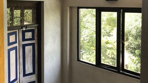 A room with a concrete wall, a window with a view of greenery, and a door with a number. - Blue Pillars Kandy (Kandy)