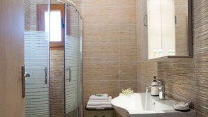 Un baño moderno con cabina de ducha de vidrio, un lavabo blanco con dispensador de jabón y un espejo sobre el lavabo.