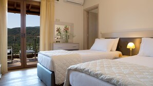 Habitación de hotel con dos camas, un balcón con vistas, una mesita con un jarrón de flores y un equipo de aire acondicionado.