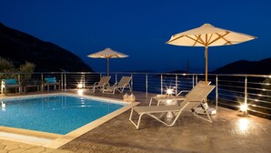 Zona junto a la piscina con sillones de descanso y sombrillas, una piscina y vistas a las montañas.
