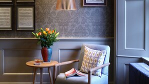 Una stanza con pavimento in legno, un divano con cuscini decorati, un tavolino con un vaso di fiori e elementi decorativi appesi alle pareti.