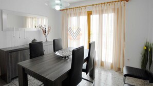 Un'area pranzo moderna con tavolo e sedie in legno, una lampada a sospensione e vista sull'esterno tramite tende leggere.