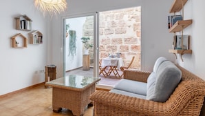 A cozy living room with wicker furniture, a glass-top coffee table, and a view of a stone wall and outdoor seating area. - House of 200 square meters in the historic center of Javea (Jávea)