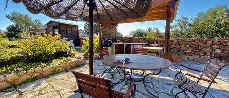 Une terrasse extérieure avec une table ronde, deux bancs en bois et un grand parasol en osier.
