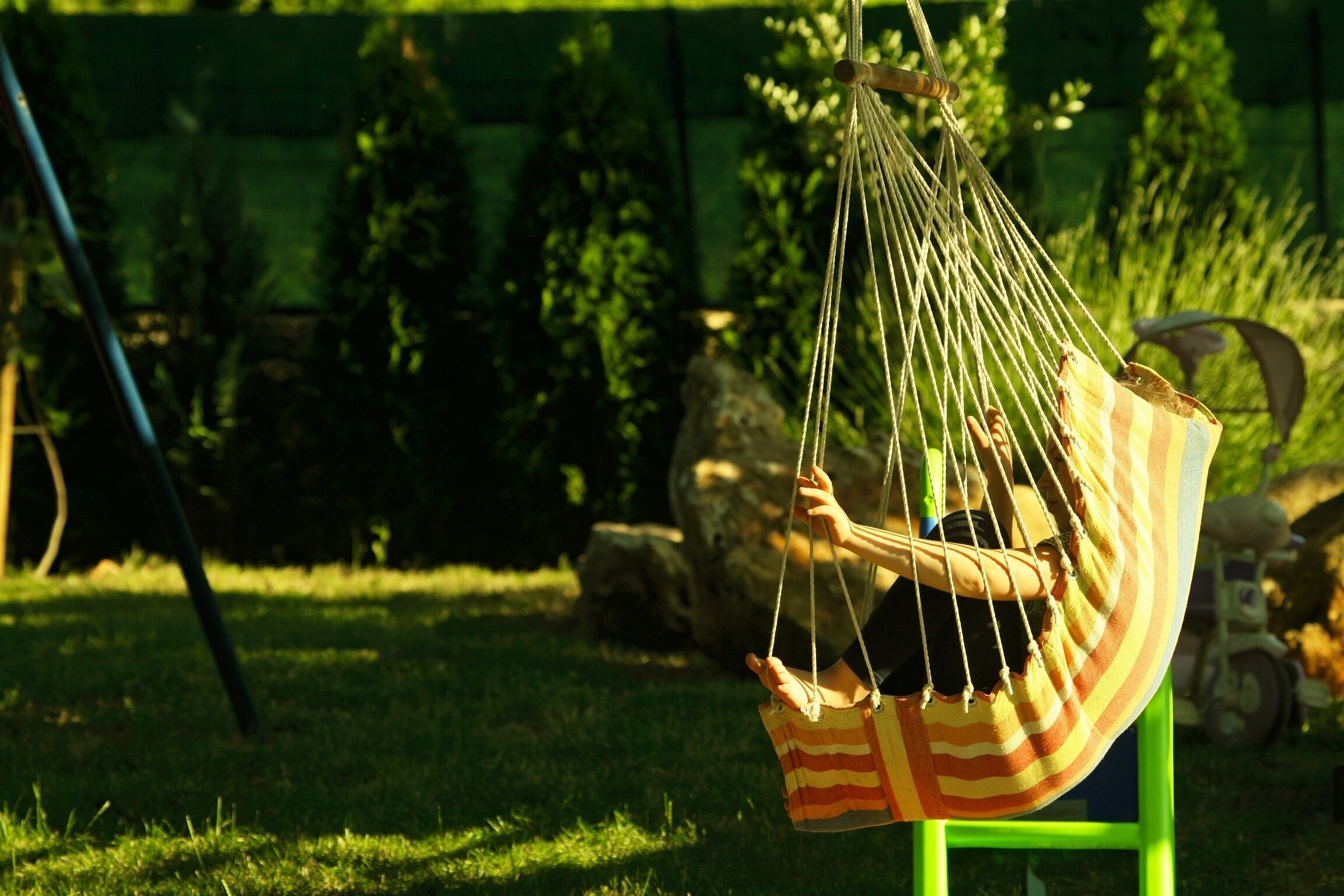 Un fauteuil suspendu en forme de hamac, maintenu par des cordes, doté d’une structure en métal vert et d’un tissu à rayures.
