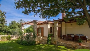 A stone house with a pergola, a patio with wooden furniture, and a well-maintained garden.