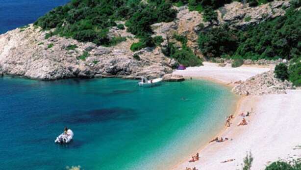 A coastal beach with clear turquoise waters, rocky terrain, and a sandy shore.
