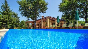 A swimming pool with clear blue water, surrounded by lounge chairs and umbrellas, with a building in the background.