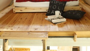 A loft bedroom with a wooden floor, a bed with red bedding, a 'Happy Holidays' pillow, and a mug on the floor. - Kl. Reetkate f. 2 pers. / WLAN / sauna / garden / a few minutes to the beach (Behrensdorf)