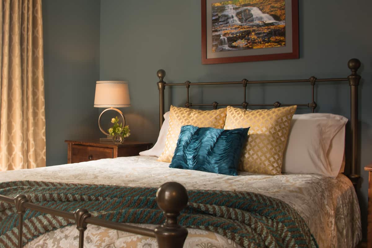 A neatly made bed with patterned bedding, a bedside table with a lamp, and a framed picture on the wall.
