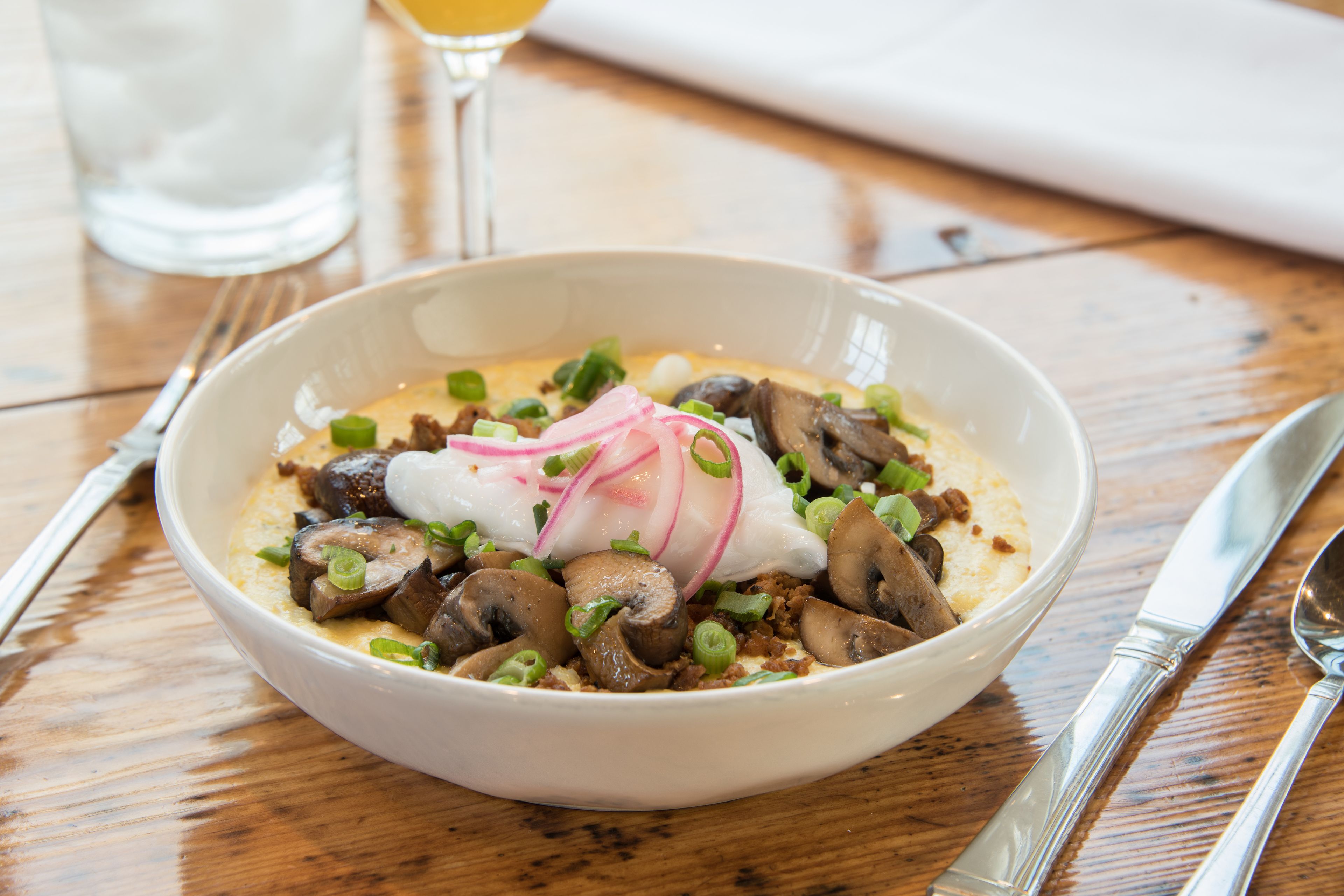 Een schaal eten met champignons en lente-uitjes op een houten tafel.