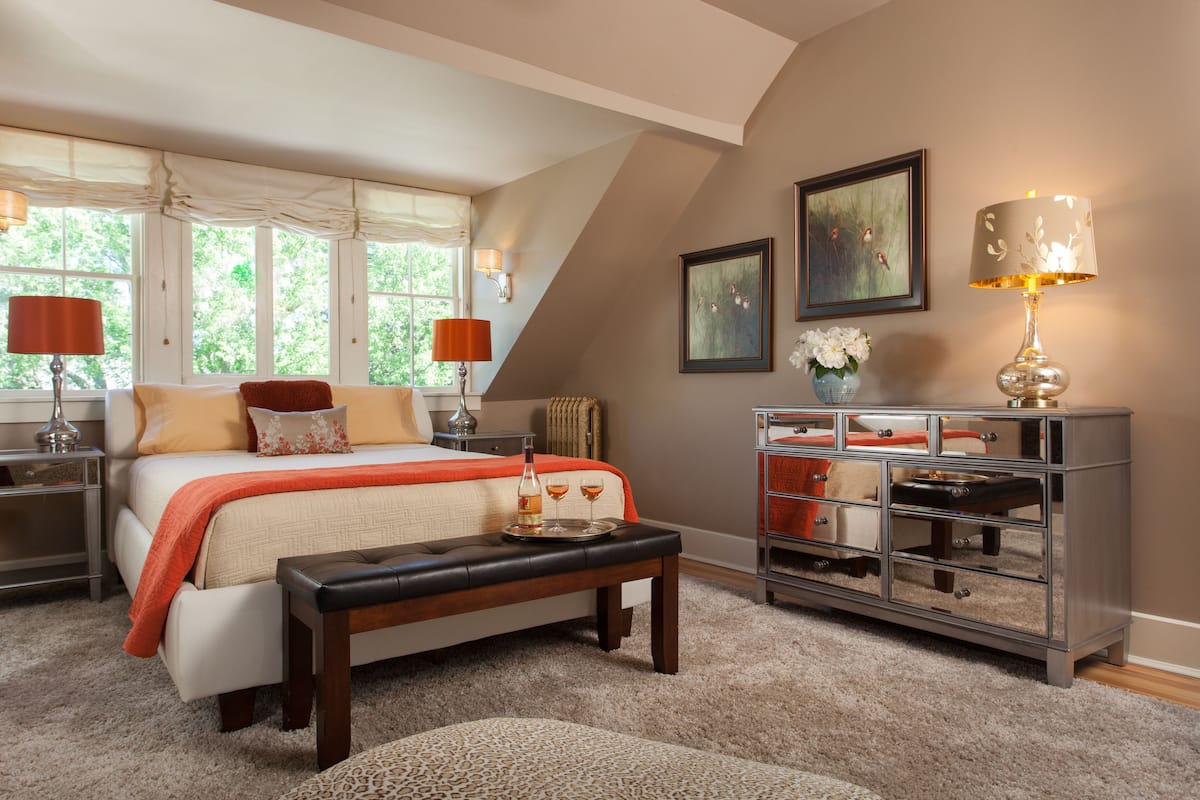 A bedroom with a bed, bedside tables, a bench, a dresser, and a window with curtains.