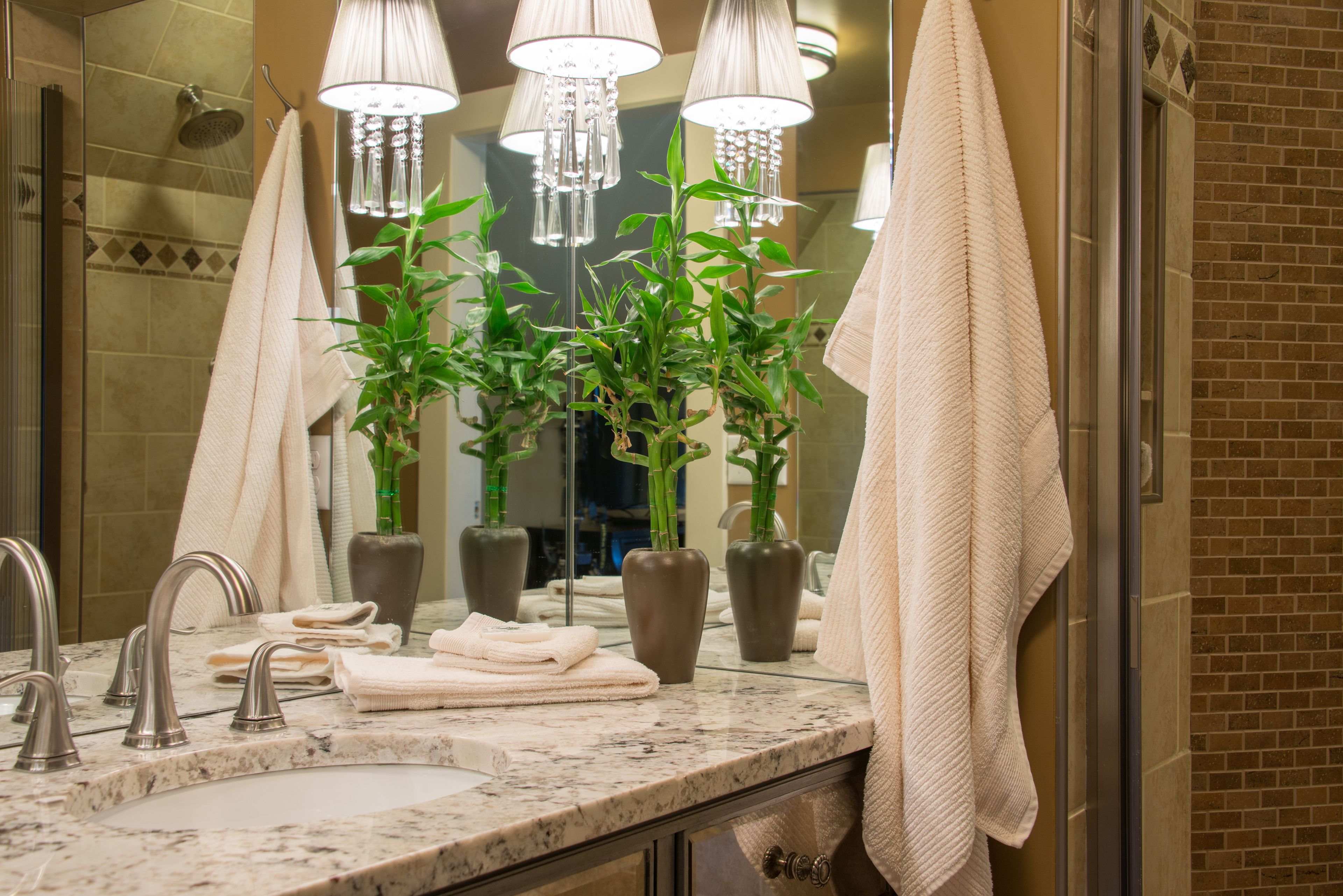 A bathroom with a marble sink, multiple towels, a large mirror, and three potted plants.