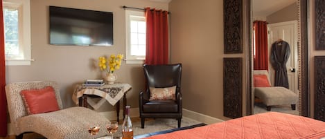 A hotel room with a bed, a chair, a table with a vase of flowers, a tray with glasses and a bottle, and a large mirror.