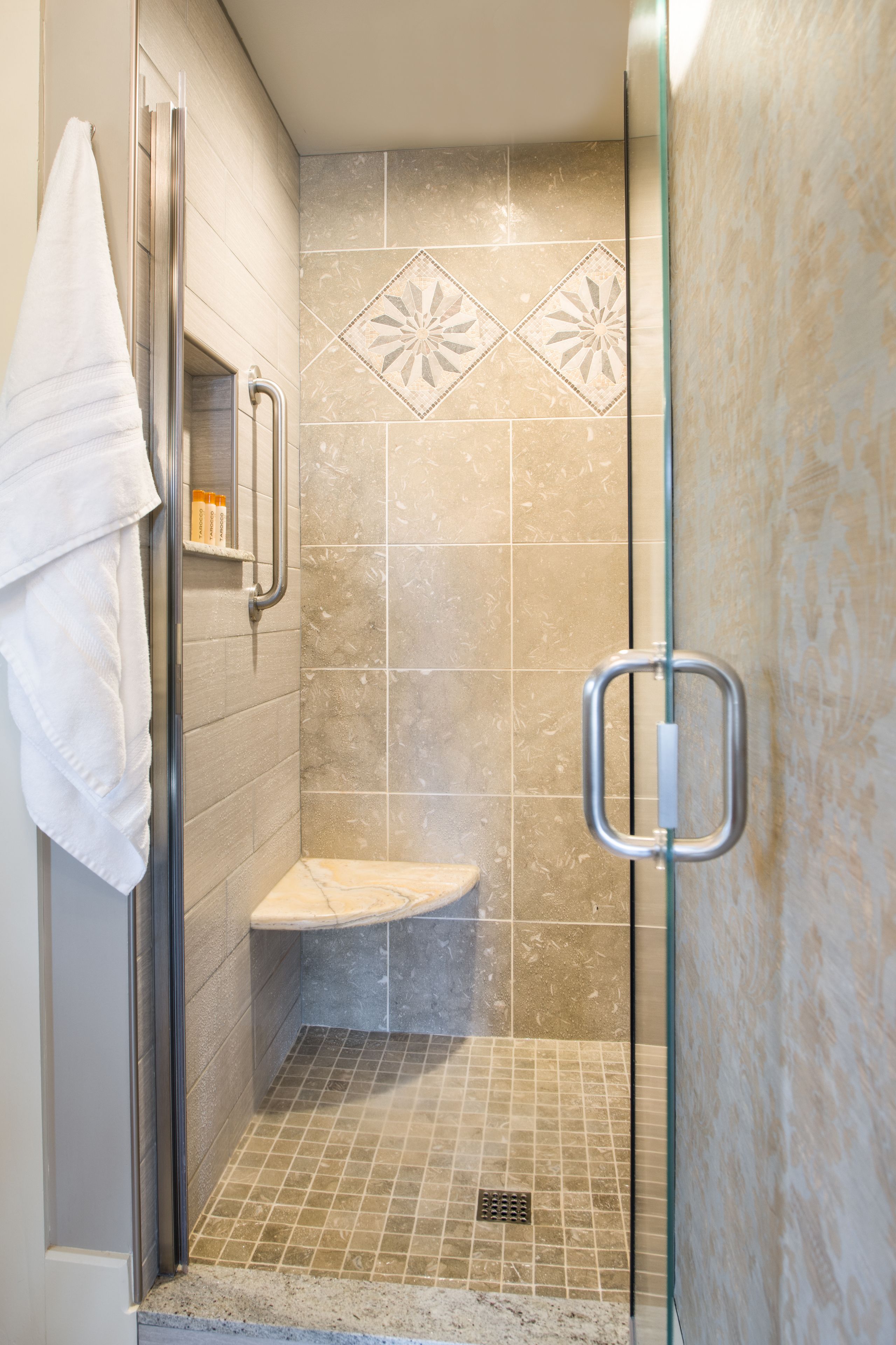 A shower stall with a glass door, a white towel hanging on the door, and a shelf with toiletries.