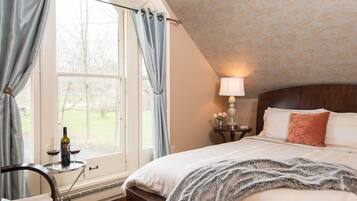 A bedroom with a large window, a bed with a fluffy blanket, a bedside table with a lamp, and a bottle of wine.