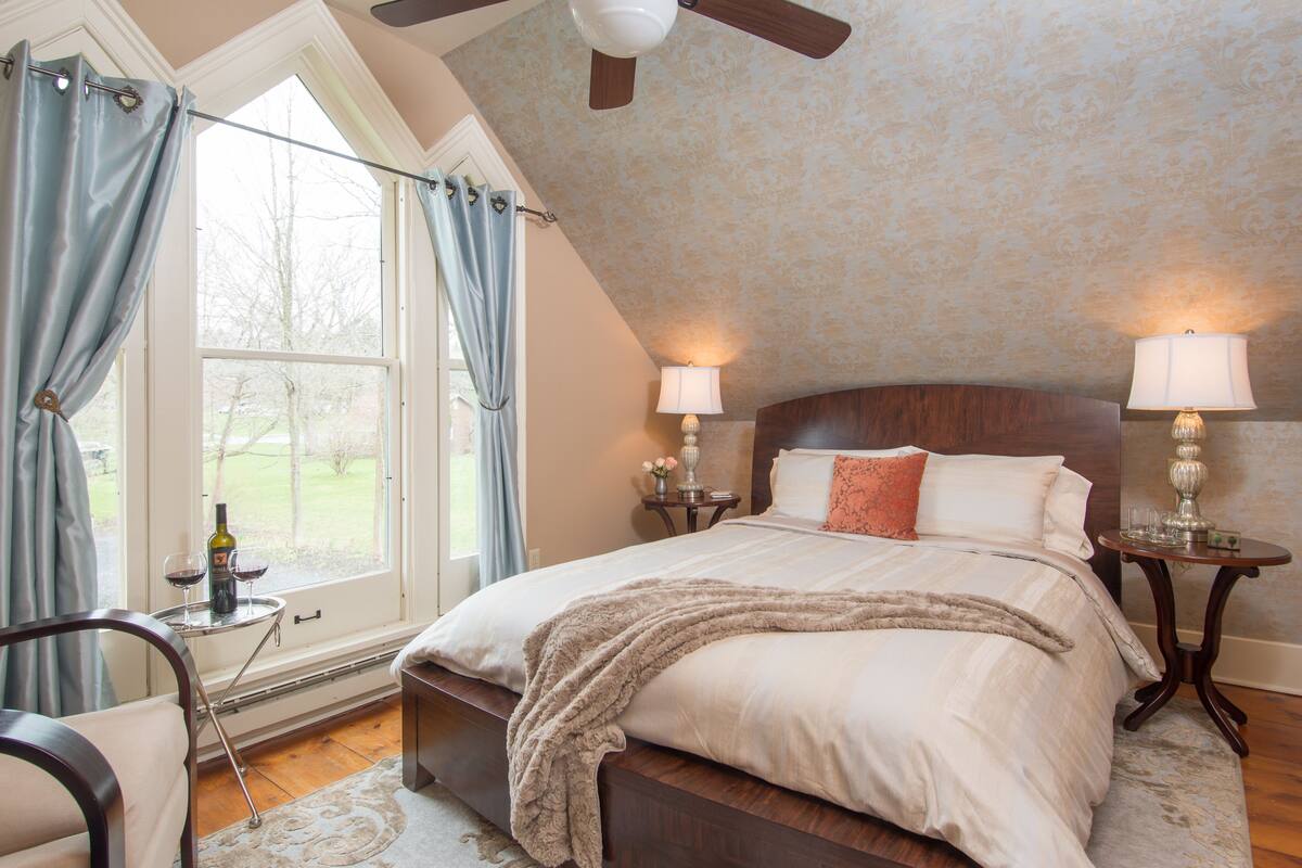 A bedroom with a large bed, two bedside tables with lamps, a window with curtains, and a ceiling fan.