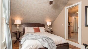 A bedroom with a sloped ceiling, a bed with a headboard, two bedside tables with lamps, and a mirror on the wall.