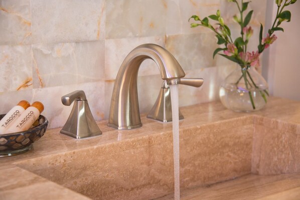 A bathroom with a modern faucet, a bowl of toiletries, and a vase with flowers.