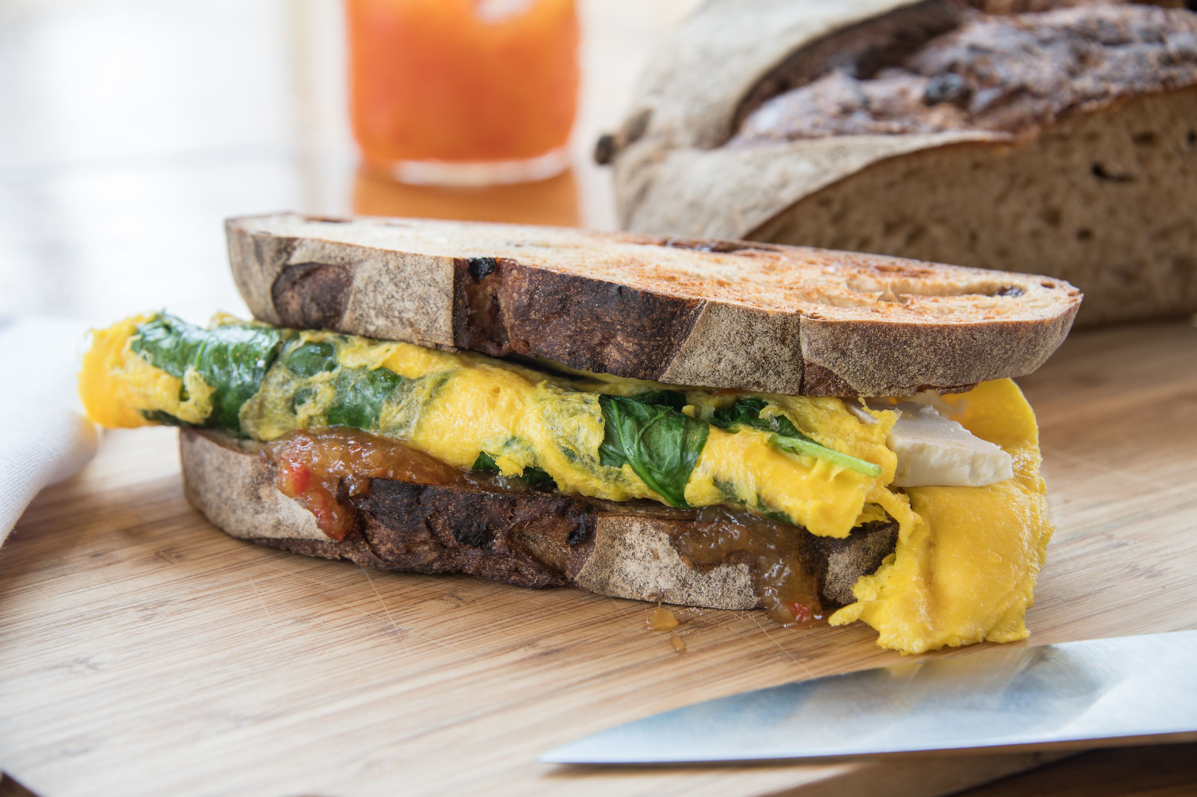 A sandwich with egg and spinach on a slice of whole grain bread, placed on a wooden cutting board.