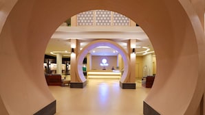 Una zona de recepción de hotel con diseño moderno, que incluye un mostrador central, un techo decorativo y un vestíbulo espacioso.
