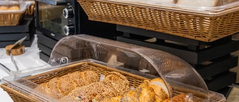 A bakery display with various types of bread and pastries in wicker baskets and plastic containers.