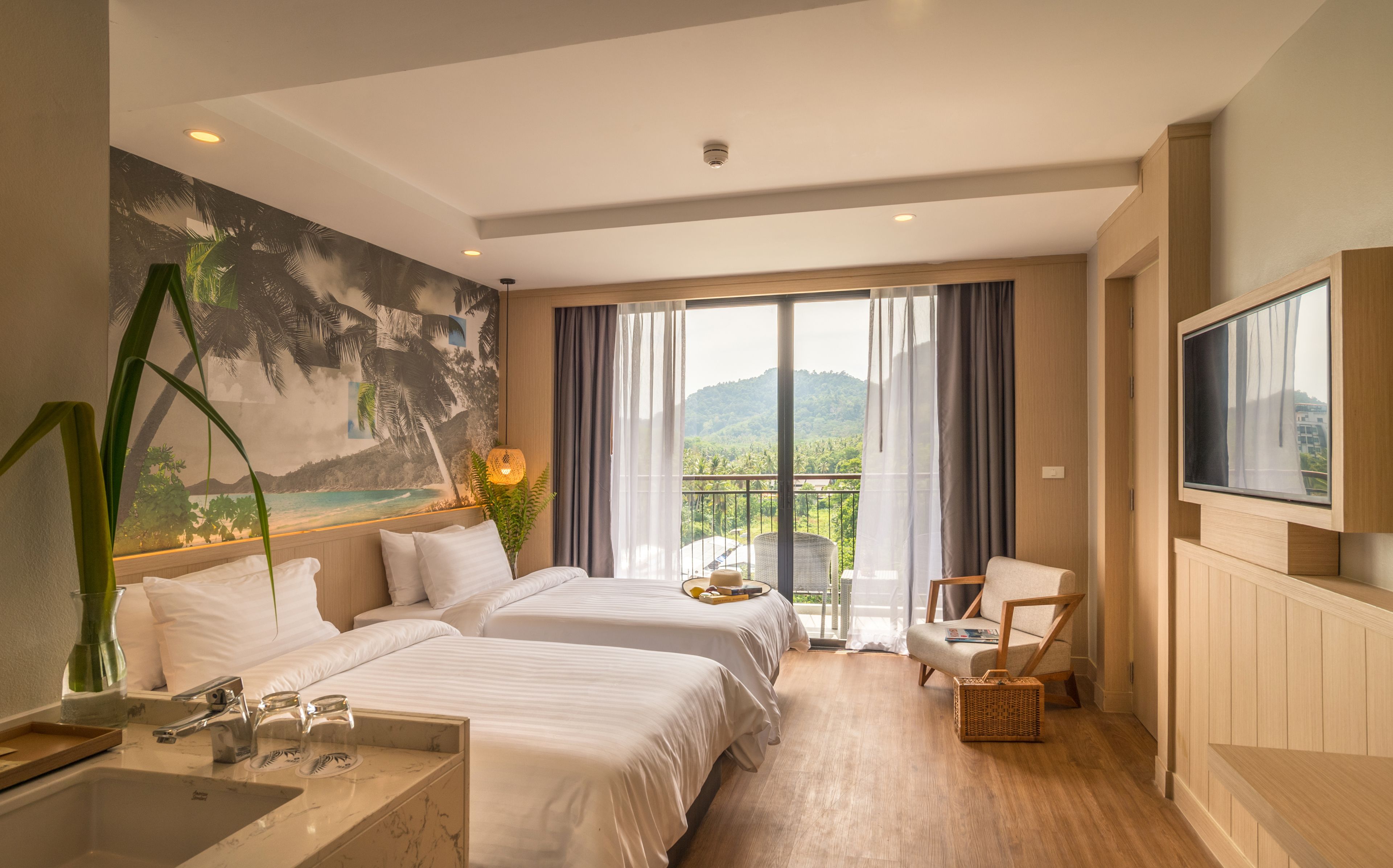 A hotel room with two beds, a TV, a balcony with a view of the mountains, and a painting of a beach scene.
